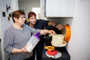 Eine Frau wiegt Mehl ab, eine weitere unterstützt sie dabei.