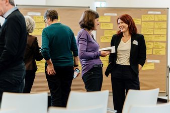 Tagungsteilnehmerinnen tauschen sich aus, im Hintergrund Pinnwände mit gelben Karteikarten.
