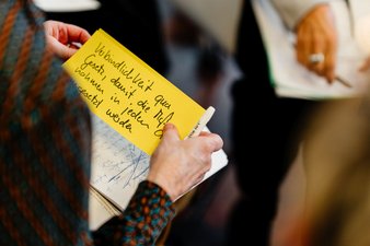 Hände, die eine gelbe, beschriebene Karteikarte festhalten.