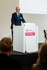 Michael Brand, Parlamentarischer Staatssekretär des BMBFSFJ Christian Luft steht an einem Pult und hält ein Grußwort.