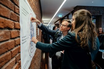 Zwei Personen kleben Punkte auf ein Poster, um Feedback zur Tagung zu geben.