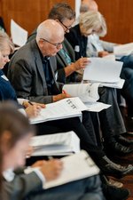 Die Teilnehmenden im Plenum markieren sich wichtige Punkte im ausgegebenen Konzept.