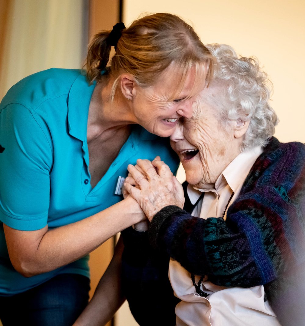 Eine Pflegeperson und eine Seniorin lachen zusammen. 