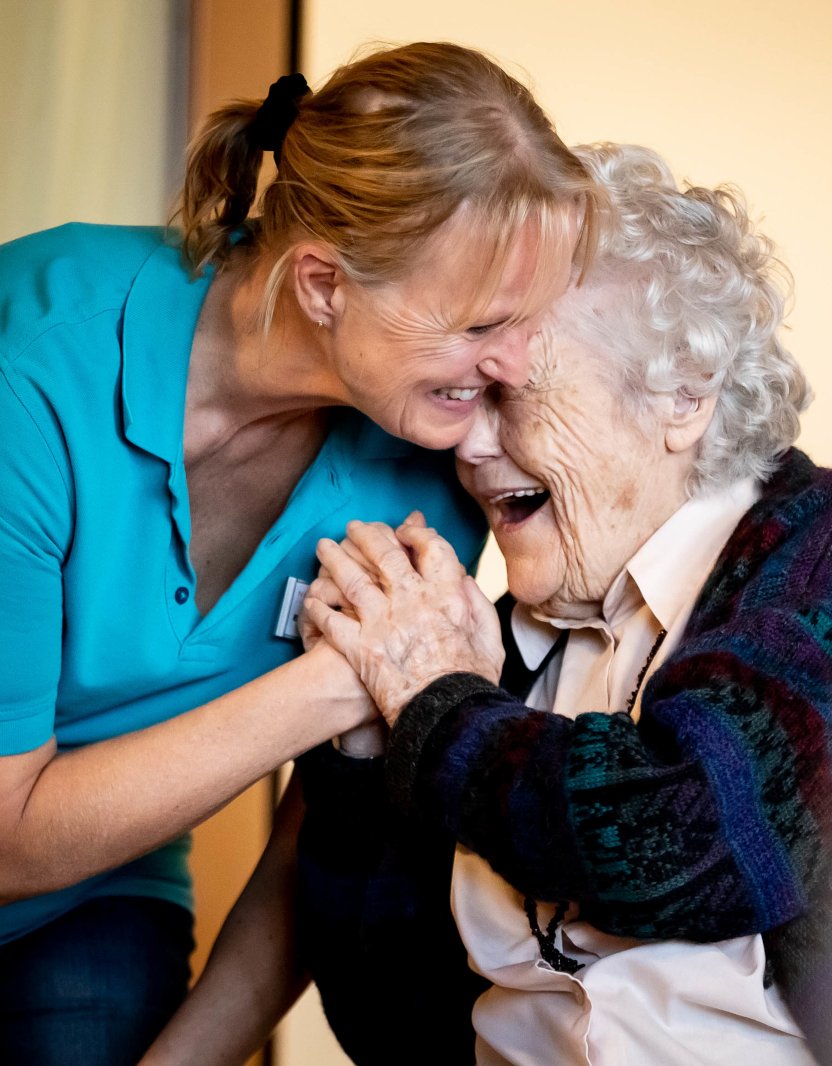 Eine Pflegeperson und eine Seniorin lachen zusammen. 