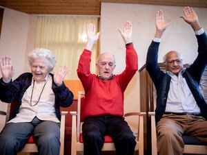 Drei ältere Personen heben beim Sitztanz die Hände