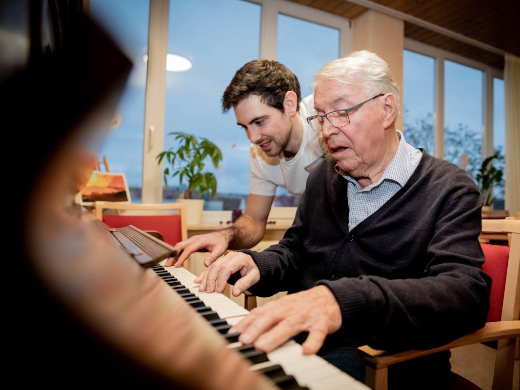 Ein älterer und ein jüngerer Mann spielen gemeinsam Klavier