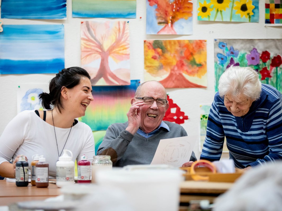 Eine Kunsttherapeutin und zwei ältere Menschen lachen gemeinsam
