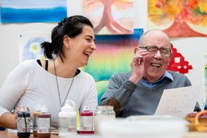 Eine Kunsttherapeutin und zwei ältere Menschen lachen gemeinsam