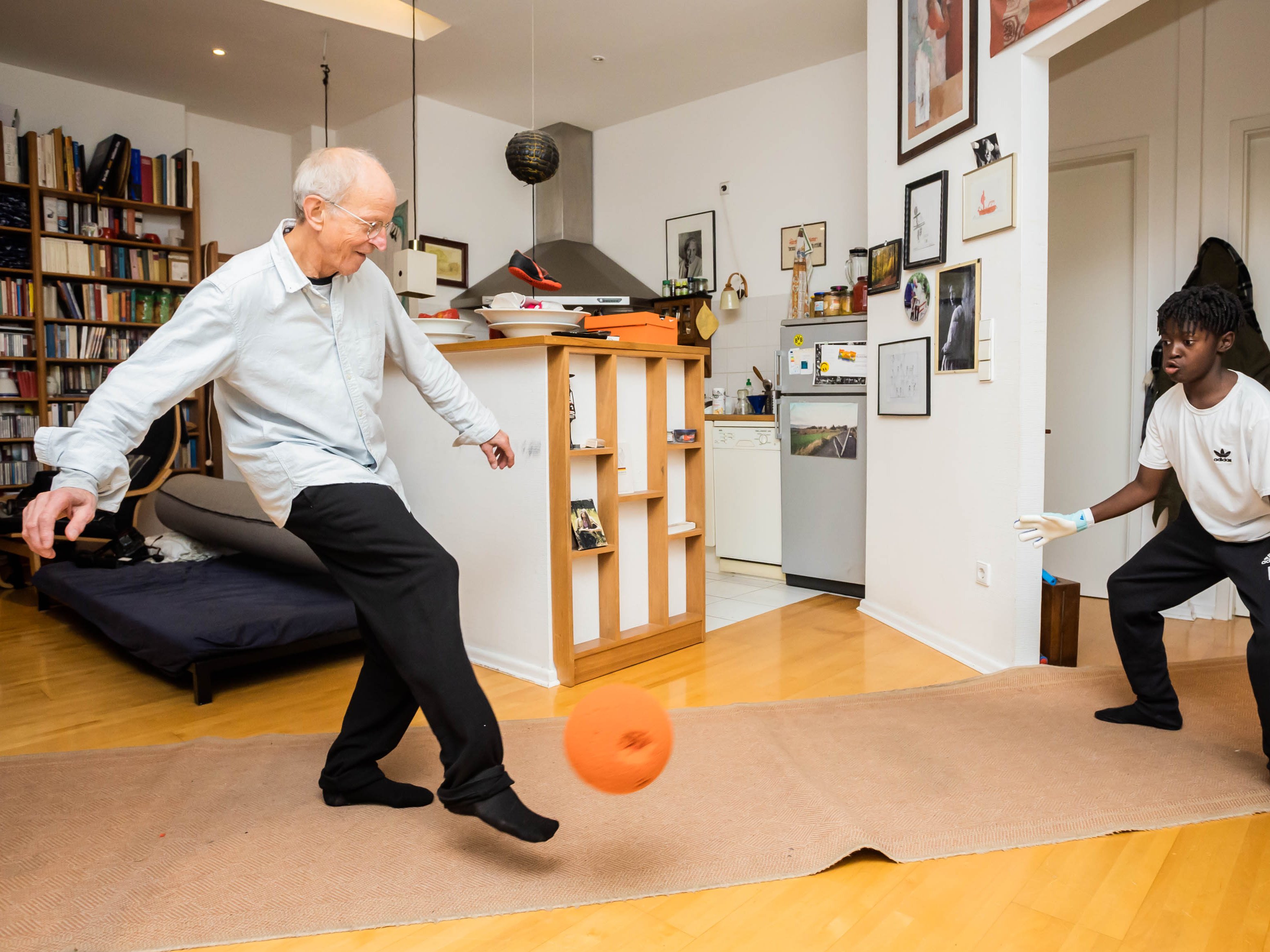 Ein älterer Mann spielt mit einem Kind Fußball in der Wohnung.
