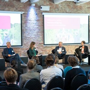 Eine Podiumsdiskussion bei der Netzwerktagung der Nationalen Demenzstrategie. Auf dem Bild sind vier Redner:innen zu sehen.