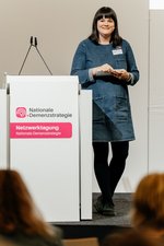 Astrid Lärm (Geschäftsstelle Nationale Demenzstrategie) lehnt sich an der Bühne an das Posium mit der Aufschrift "Nationale Demenzstrategie"