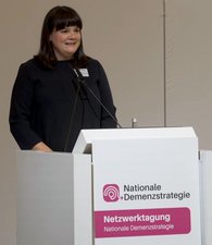 Astrid Lärm, Leiterin der Geschäftsstelle Nationale Demenzstrategie, begrüßt das Publikum mit einer kurzen Rede an einem Pult.