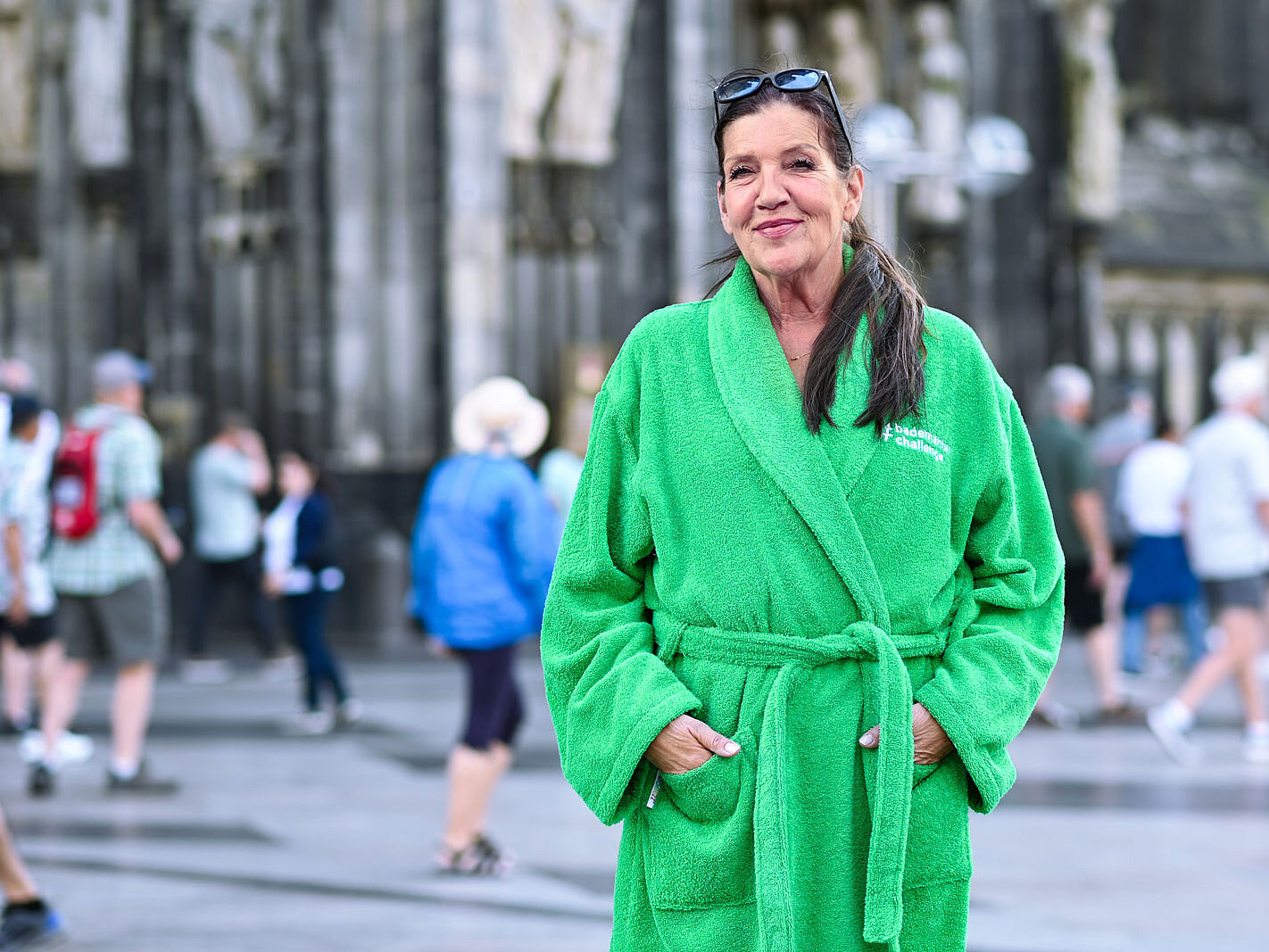 Schauspielerin Katy Karrenbauer im grünen Bademantel vor dem Kölner Dom, sie beteiligt sich an der Bademantelchallenge.