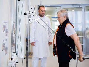 Eine ältere Frau nutzt unter Aufsicht eines Arztes ein Gerät zum Training der Armmuskulatur. © DZA/Christoph Soeder