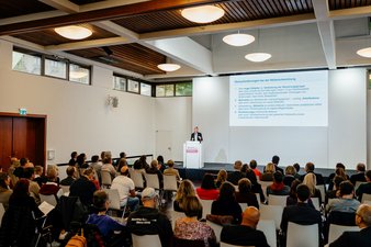 Publikum und Podium mit Dr. Christine Schwendner, die einen Vortrag zur Bayerischen Demenzstrategie hält.