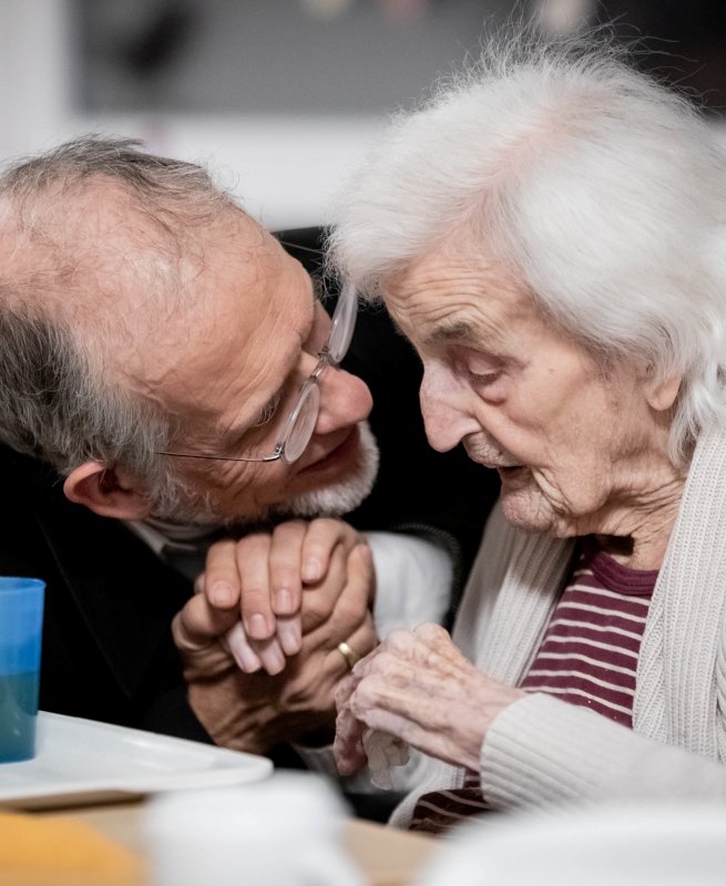 Älterer Mann und Seniorin, älterer Mann hält die Hand der Seniorin und schaut ihr bestärkend ins Gesicht.