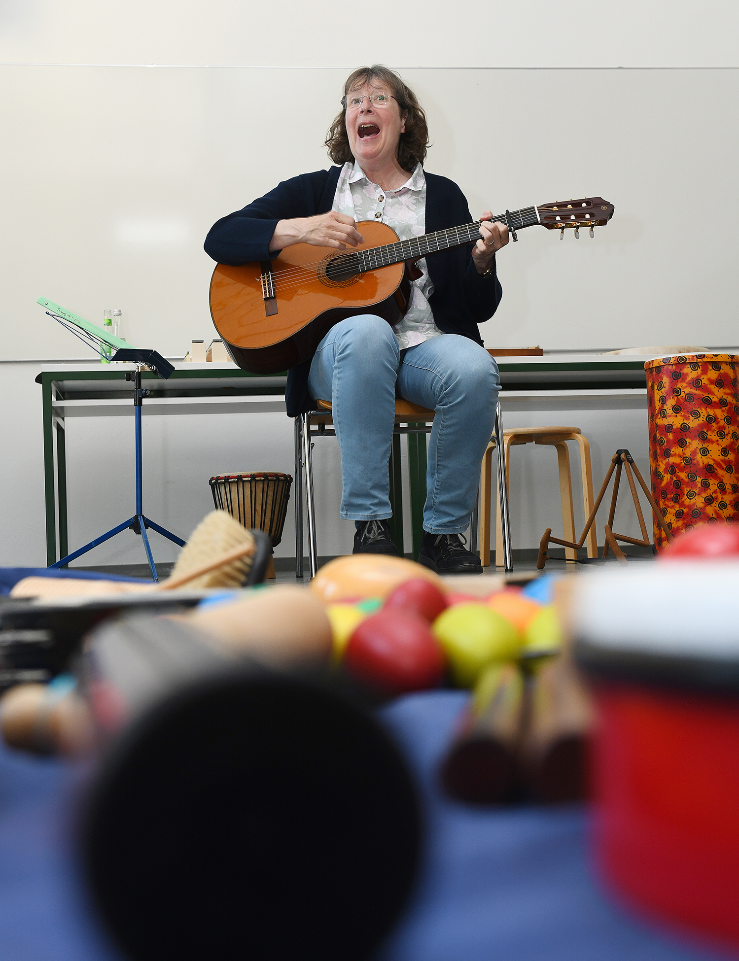 Eine Frau spielt Gitarre, vor ihr auf dem Boden liegen Rhythmus-Instrumente.