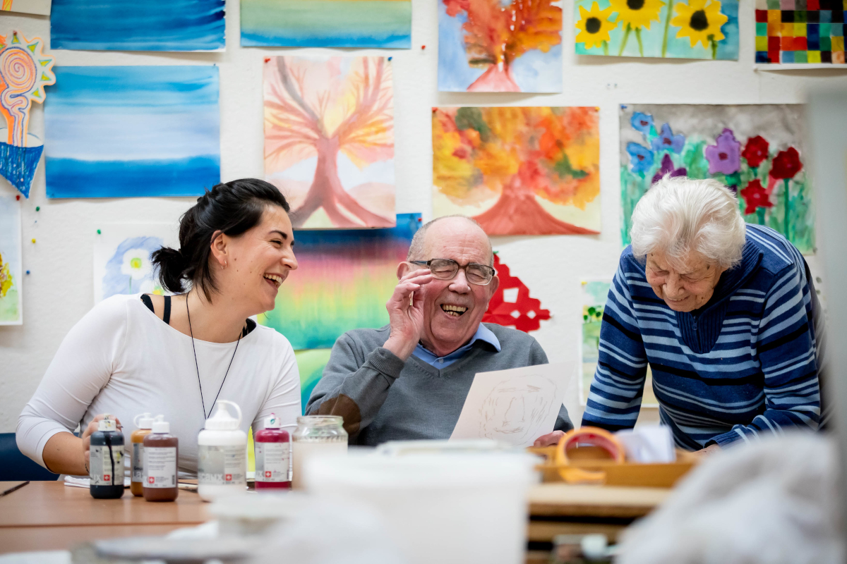 Eine Kunsttherapeutin und zwei ältere Menschen lachen gemeinsam